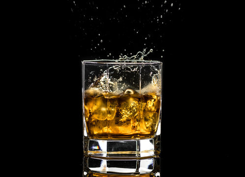 Hexagonal glass of whiskey brandy with ice and splashes from falling ice