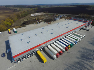 Aerial view of goods warehouse. Logistics center in industrial city zone from above. Aerial view of trucks loading at logistic center