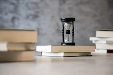 Klepsydra stojąca na książkach, pomiedzy książkami na szarym tle © andsko