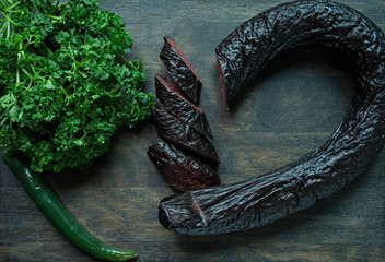 Blood sausage on a dark cutting board decorated with curly parsley. Blood sausage. View from above....