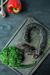 The blood sausage on a dark cutting board is decorated with fresh herbs and vegetables. Blood...