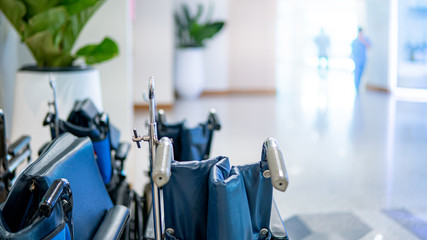 Group of blue folding wheelchair with blurred doctor and nurse walking through the corridor in hospital or medical clinic. Healthcare and medical service concept