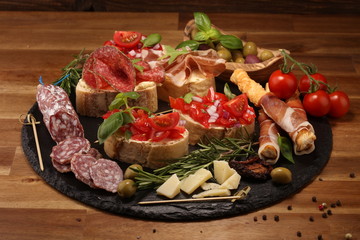 Traditional italian antipasto bruschetta appetizer with cherry tomatoes, cream cheese, basil leaves and balsamic vinegar on cutting board with prosciutto, salami, cheese