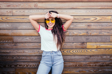 Young positive girl student in stylish clothes is posing against the background of a wooden wall and is enjoying first warm summer days. Place for text