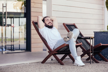 Happy young stylish hipster man with beard resting sitting on the lounge beside the hotel. Concept...