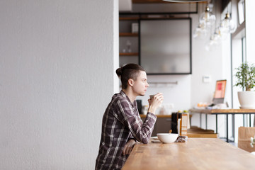 Side view - young handsome man looks at computer and drinks coff