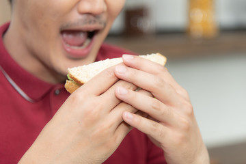 Asian smiling young man with casual  red t-shirt enyoy having breakfast, eating sandwich, Young man cooking food and drink in the loft style kitchen room