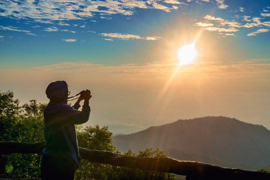 Tourism vacation and travel. A tourist taking photo of beautiful sun rise at mountain landscape at sun rise time with mirrorless camera at Doi Ang Khang, Thailand
