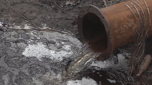 Chemically dirty water gushing from a large rusty pipe in the river, formed foam. Water pollution. Super slow motion 1000 fps
