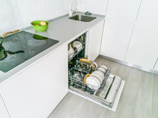 Open dishwasher with clean dishes in the white kitchen