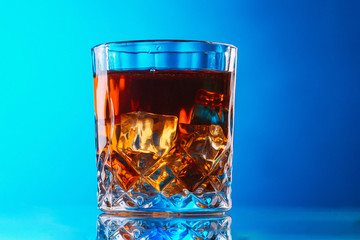 Whisky on lowball glass with ice over reflective surface