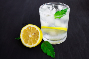  A glass of cold water with about ice, lemon and mint on a blue background