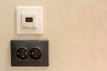 Double electric isolated socket and thermostat installed on light yellow plastered wall. Power...