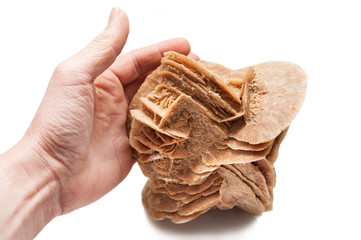 Hand on a white background holds a desert rose formed from sand in the Sahara Desert. Rock formed of sand