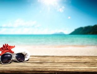 Desk of wood and free space for your decoration. White towel on top with sunglasses and red shell. Free space for your product and landscape of ocean with small island. 