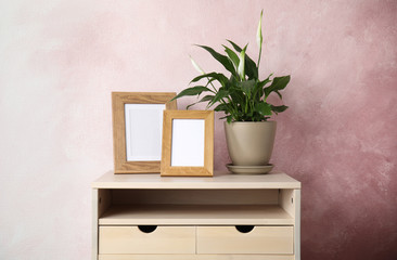 Spathiphyllum plant and photo frames on table near color wall, space for design. Home decor