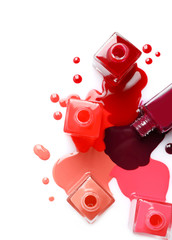 Spilled different nail polishes with bottles on white background, top view