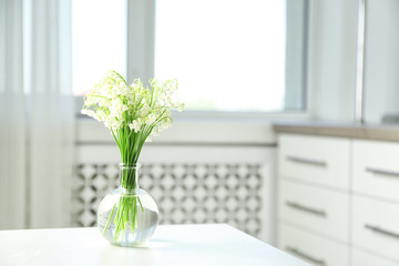 Vase with beautiful lily of the valley bouquet on table in room, space for text