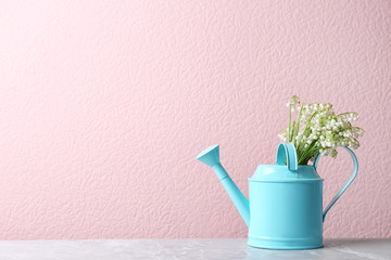 Beautiful lily of the valley bouquet in watering can on table near color wall, space for text