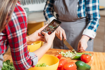Cooking blog. Two women making salad cutting vegetables taking smartphone pictures. Healthy nutrition vegan lifestyle.