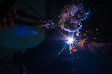 Worker with protective gloves welding metal part in workshop