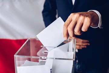 Man throwing his vote into the ballot box. Polish flag in the background.