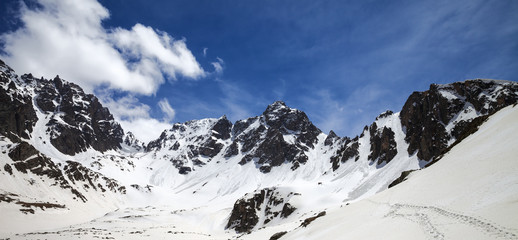 Panoramic view on snowy sunlight mountains and cloudy blue sky