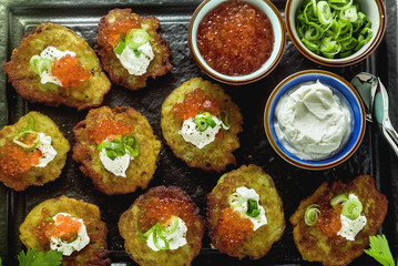 Russian traditional potato pancakes served with red caviar, green onions and sour cream on a tray with white wine and lemon