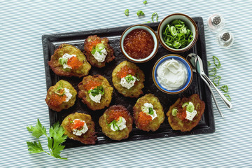 Russian traditional potato pancakes served with red caviar, green onions and sour cream on a tray with white wine and lemon