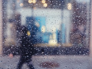 a blurry silhouette of a person walking behind a wall of raindrops on a city sidewalk