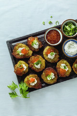 Russian traditional potato pancakes served with red caviar, green onions and sour cream on a tray with white wine and lemon
