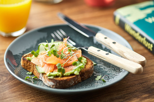 Close-up of toast with fish and avocado with greens on plate.