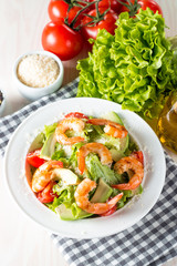 Fresh shrimp salad made of tomato, ruccola, avocado, prawns, chicken breast, arugula, crackers and spices. Caesar salad in a white, transparent bowl on wooden background
