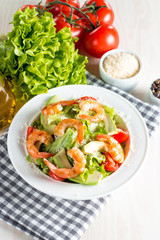 Fresh shrimp salad made of tomato, ruccola, avocado, prawns, chicken breast, arugula, crackers and spices. Caesar salad in a white, transparent bowl on wooden background