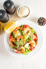 Fresh shrimp salad made of tomato, ruccola, avocado, prawns, chicken breast, arugula, crackers and spices. Caesar salad in a white, transparent bowl on wooden background