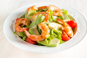 Fresh shrimp salad made of tomato, ruccola, avocado, prawns, chicken breast, arugula, crackers and spices. Caesar salad in a white, transparent bowl on wooden background