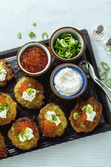 Russian traditional potato pancakes served with red caviar, green onions and sour cream on a tray with white wine and lemon
