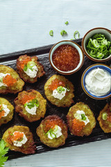 Russian traditional potato pancakes served with red caviar, green onions and sour cream on a tray with white wine and lemon
