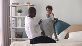 Happy african dad and son having pillow fight on bed
