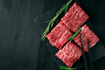 Sliced wagyu marbled beef for yakiniku on plate on black background, Premium Japanese meat and stick, top view and copy space