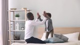Happy child son jumping playing with black father on bed