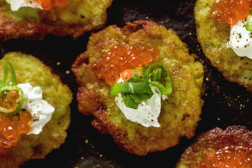 Russian traditional potato pancakes served with red caviar, green onions and sour cream on a tray with white wine and lemon