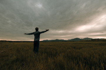 Young man standing in meadow under thunder sky