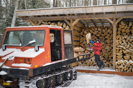 Boy at wood shed has fun tossing firewood into bed of vintage orange snow groomer