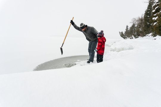 Father and son together on snowy adventure using shovel to break ice