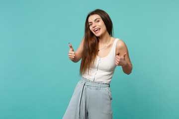 Cheerful funny young woman in light casual clothes looking camera, showing thumbs up isolated on blue turquoise background in studio. People sincere emotions, lifestyle concept. Mock up copy space.