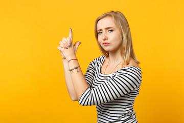 Attractive young woman in striped clothes looking camera, holding hands like gun isolated on yellow orange wall background in studio. People sincere emotions, lifestyle concept. Mock up copy space.