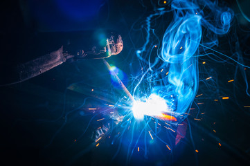 Worker with protective gloves welding metal part in workshop