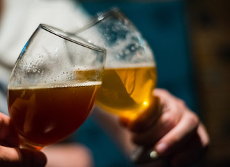 Close-up view of a two glass of beer in hand. Beer glasses clinking in bar or pub