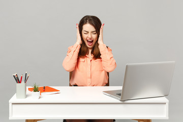 Young screaming woman in pastel clothes keeping eyes closed, hold hands near head sit, work at desk with pc laptop isolated on gray background. Achievement business career concept. Mock up copy space.